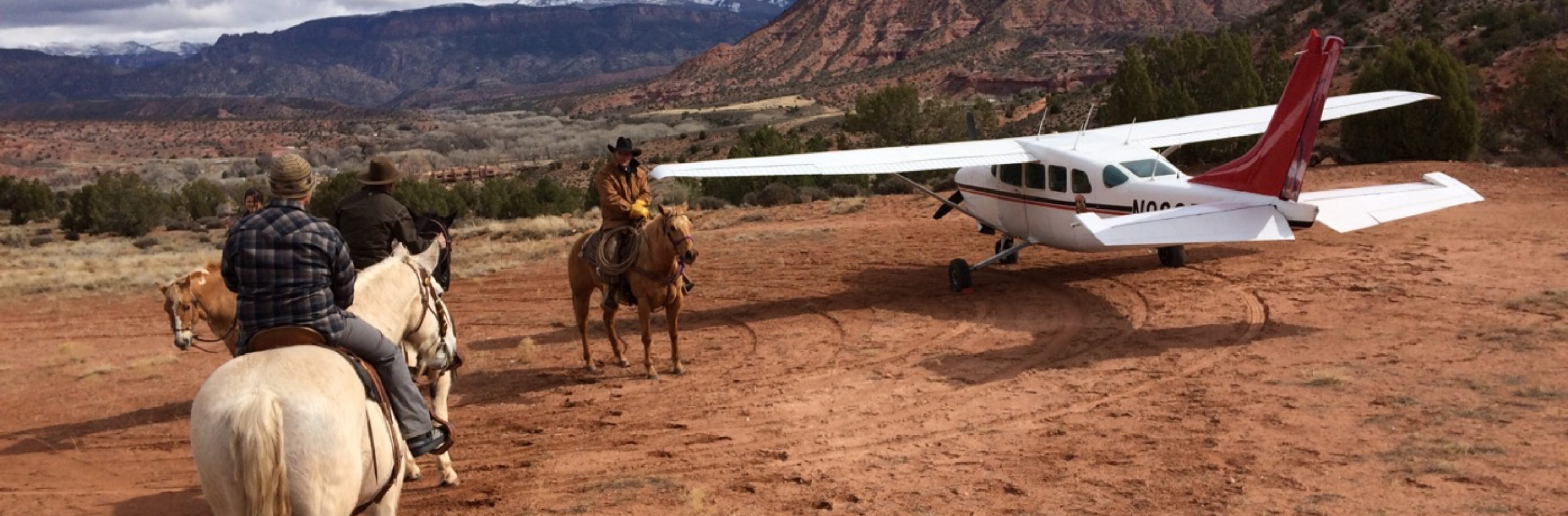 Three people on horses next to a plane in Moab