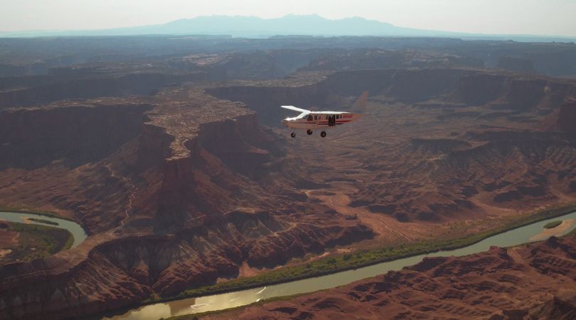 small white airplane flying over a river in utah