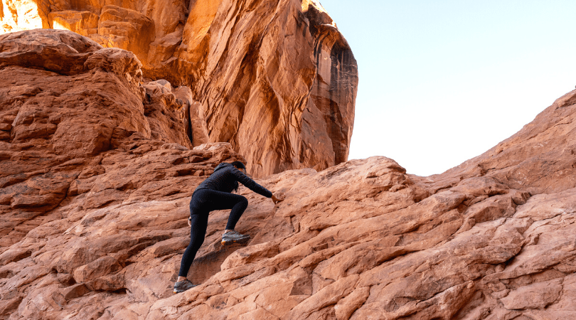 person climbing red rocks in desert