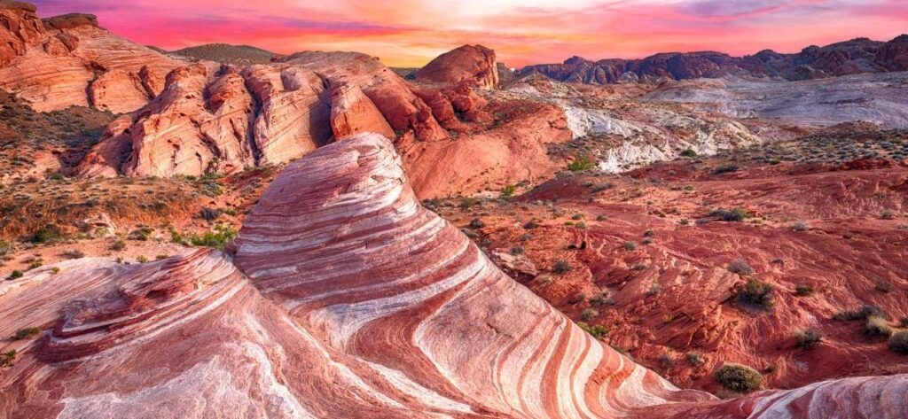 wavy patterns on red rocks in front of pink sunset