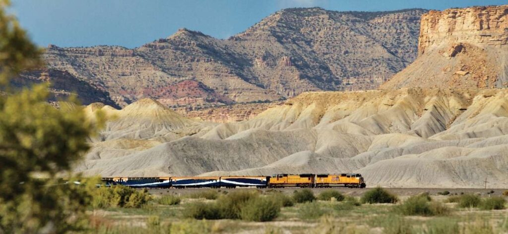 yellow train in front of colorful rocky mountains