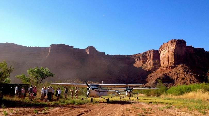 group of people standing outside a landed airplane in the desert