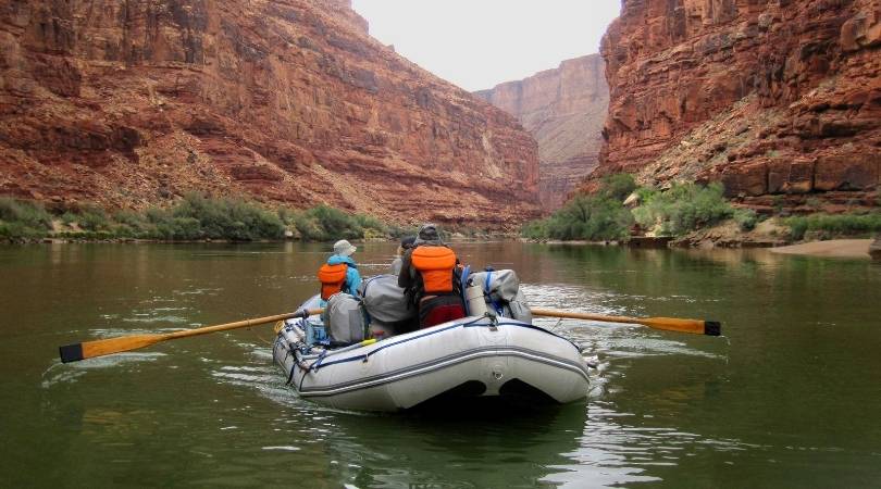 group rowing a raft down a canyon river