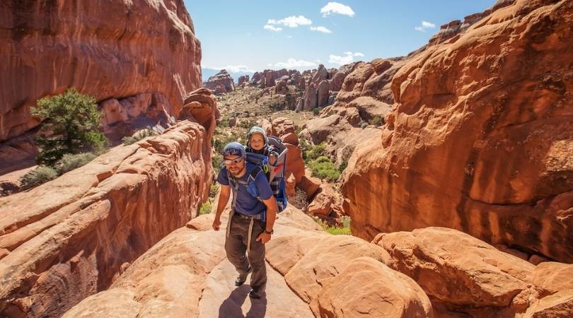 man hiking with young child in backpack