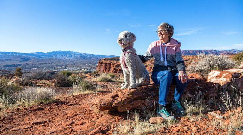 woman and dog sitting on a rock looking out