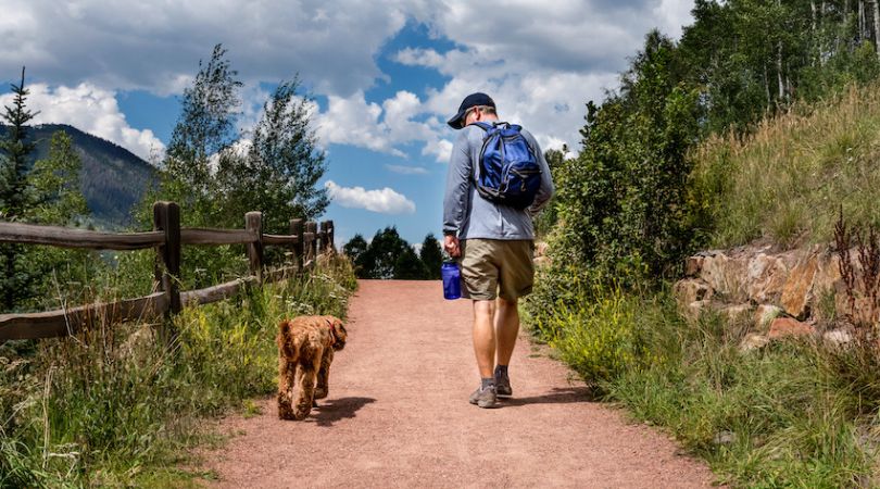 man hiking next to a dog on a trail