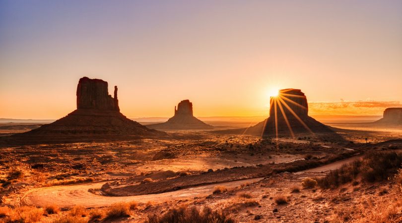 sun rising behind a rock tower in monument valley