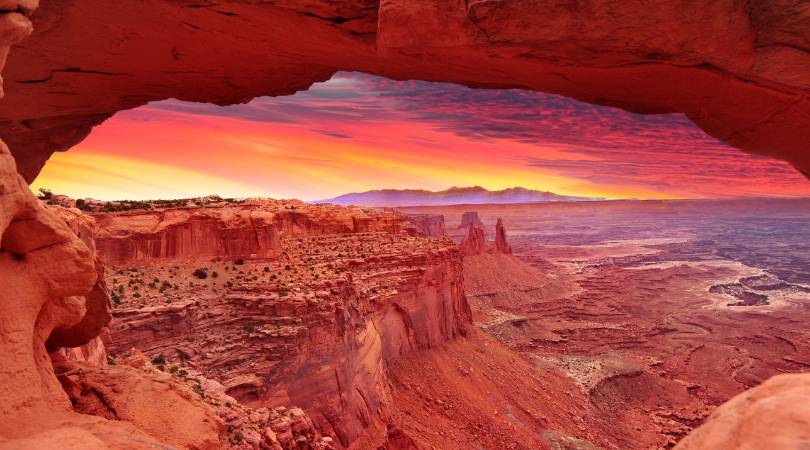 brilliant pink and yellow sky through an arch in canyonlands