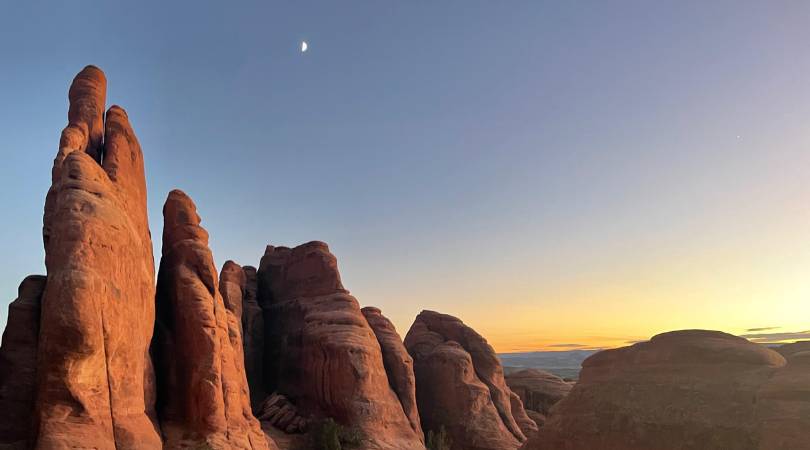 the moon above red rock towers at sunset