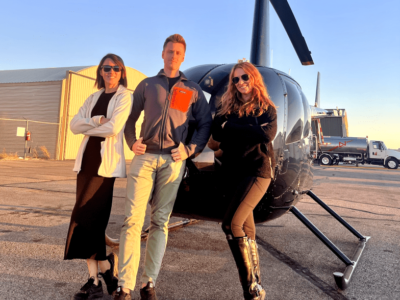 3 people in front of a black helicopter ready for a helicopter tour of moab and canyonlands