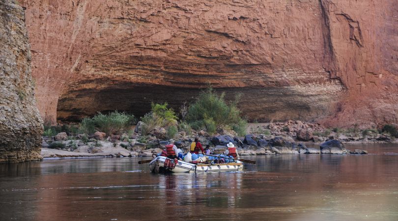 people on a raft admiring tall red rock canyon walls