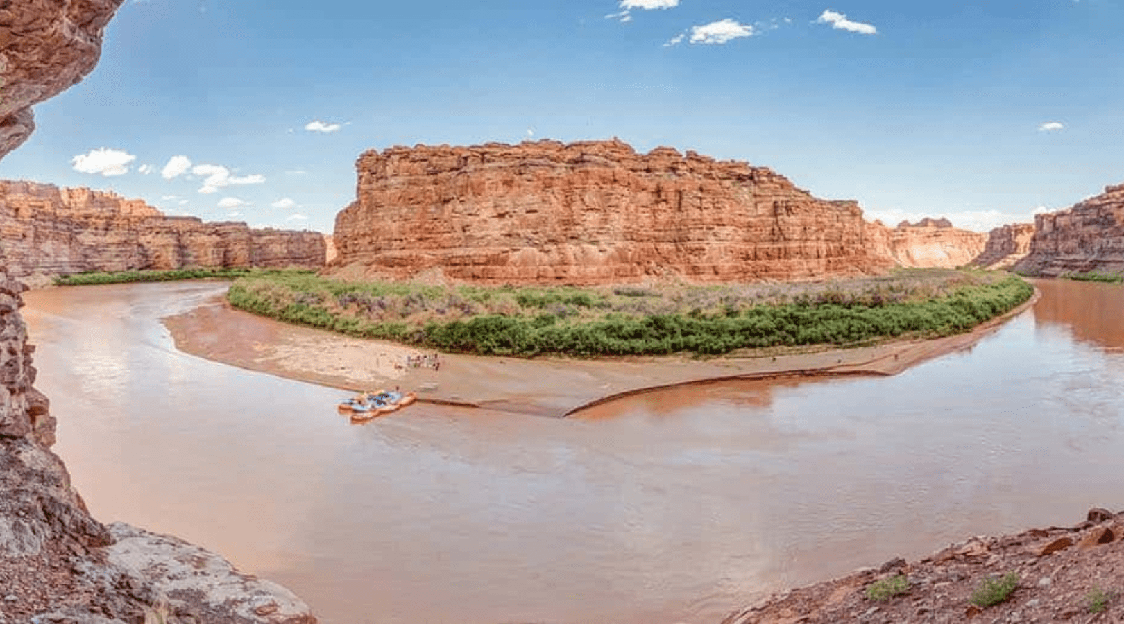 views from across the colorado river of rafts shored up in cataract canyon with red rock canyon walls in the back